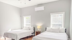Et soveværelse med to senge, et sengebord med en lampe og et vindue med persienner.