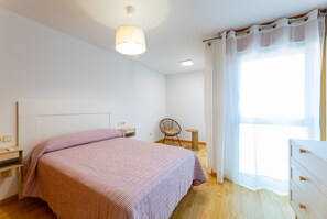A bedroom with a bed, bedside tables, a chair, a small table, a lamp, and a window with curtains. - Volvoreta Valdoviño Apartment (Valdoviño)