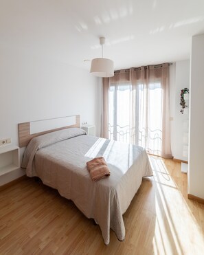 Une chambre à coucher avec un lit, des tables de chevet, une lampe suspendue et une fenêtre avec des rideaux.