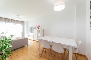 A modern living room with a sofa, dining table, chairs, and a potted plant. - Volvoreta Valdoviño Apartment (Valdoviño)