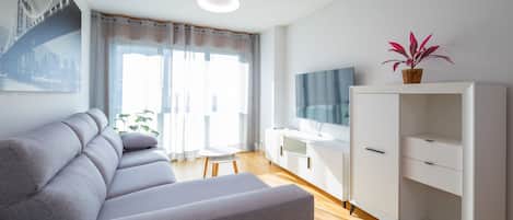 A modern living room with a grey sofa, a white TV stand, and a wooden floor.