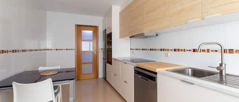 Una cocina moderna con armarios blancos, encimera de madera, lavavajillas y un comedor con mesa y sillas.