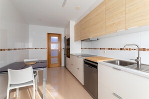 A modern kitchen with white cabinets, a wooden countertop, a dishwasher, and a dining area with a table and chairs. - Volvoreta Valdoviño Apartment (Valdoviño)