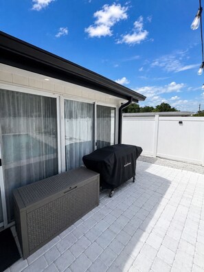 A covered outdoor seating area with a table and chairs, a covered grill, and a view of a building with large windows. - Mid-Century Pool Retreat Minutes from Siesta Key Beach Sleeps 8 (Sarasota)