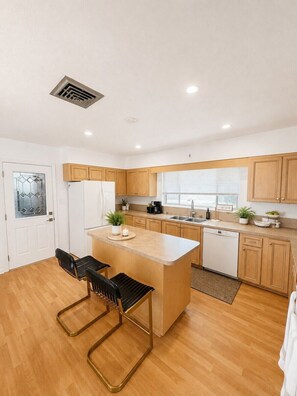 A modern kitchen with a central island, wooden cabinets, a dishwasher, and a window with blinds. - Mid-Century Pool Retreat Minutes from Siesta Key Beach Sleeps 8 (Sarasota)