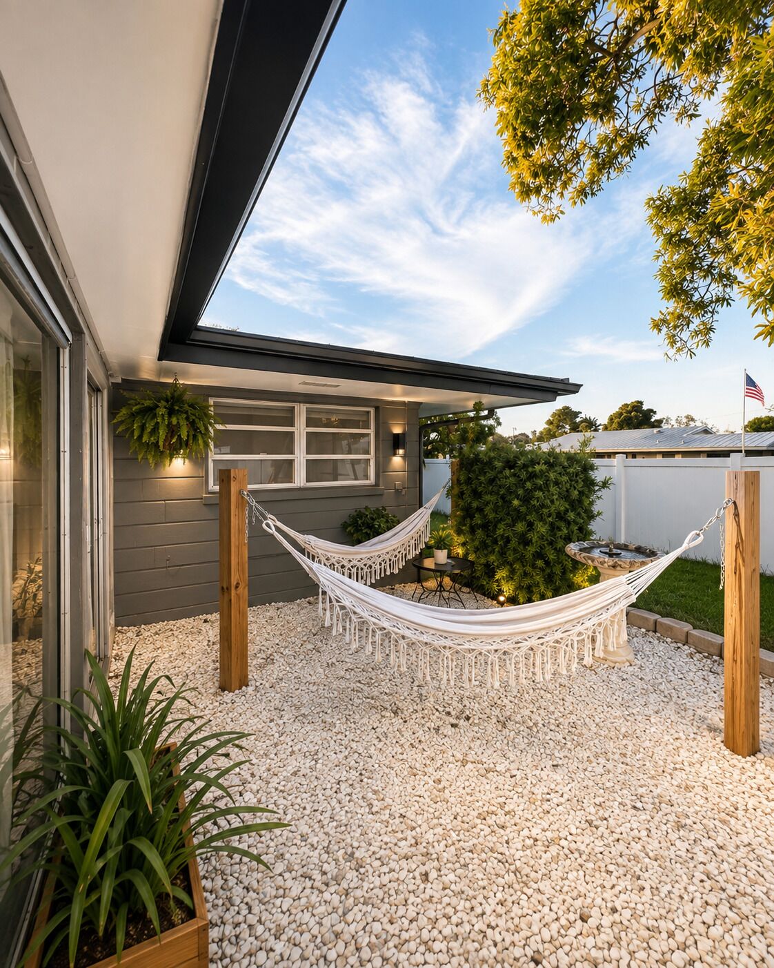 A modern house with a hammock in the backyard, surrounded by white pebbles and greenery.