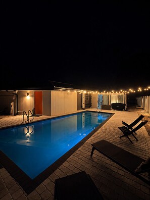 A swimming pool with a ladder, lounge chairs, and string lights at night. - Mid-Century Pool Retreat Minutes from Siesta Key Beach Sleeps 8 (Sarasota)
