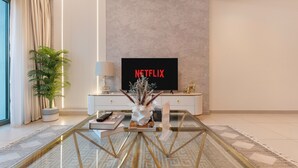 Una sala de estar moderna con una mesa de centro de vidrio, un televisor mostrando 'NETFLIX', una planta en maceta y un jarrón decorativo.