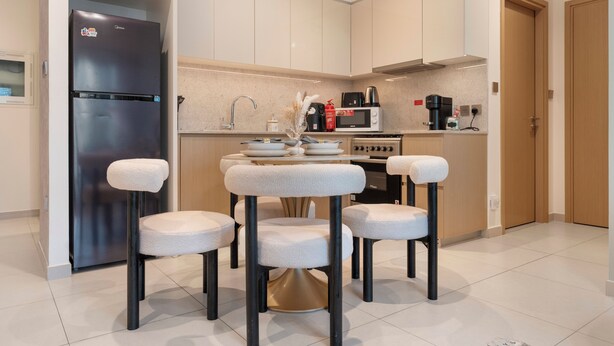 Una cocina moderna con refrigerador integrado, microondas y estufa. Hay una mesa de comedor con cuatro sillas y un florero con flores secas.