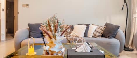 A modern living room with a glass coffee table, a sofa with patterned cushions, and a decorative vase with dried plants.