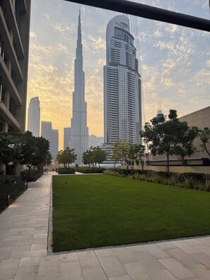 A pathway leading to a grassy area with modern buildings in the background, including a prominent tower. - Walk to Dubai Mall and Dubai Fountain Parking Pool (Dubai)