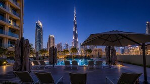 A rooftop pool area with lounge chairs and umbrellas, overlooking a city skyline with prominent skyscrapers. - Walk to Dubai Mall and Dubai Fountain Parking Pool (Dubai)