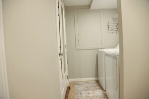 Ein schmales Korridor mit einer Tür links, einem weißen Schrank mit Handtuchhalter rechts und einem gemusterten Teppich auf dem Boden.