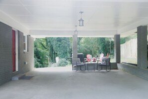 Eine überdachte Terrasse mit Betonboden, einem Tisch mit Stühlen und einem hängenden Laternenleuchter.