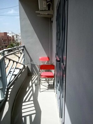 A balcony with a metal railing, a pair of red chairs, and a door with a metal grid.