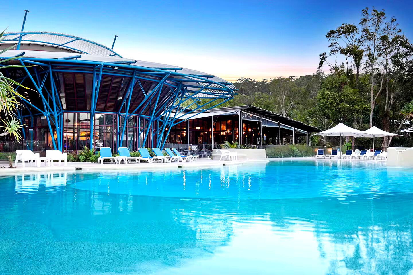Une piscine avec des chaises longues et un espace abrité comprenant des tables et des parasols.