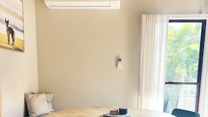 A round table with chairs, a bench with cushions, an air conditioning unit, a window with curtains, and a thermostat on the wall.