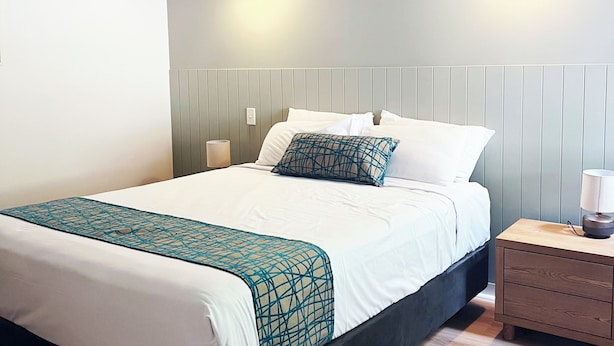 A hotel room with a bed, a nightstand, a wall-mounted air conditioner, and a ceiling fan.