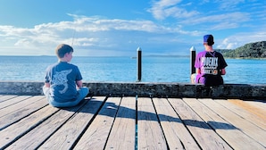 Two individuals sitting on a wooden dock overlooking a body of water with a clear sky.