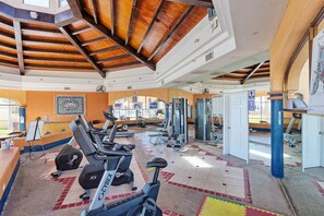 Ein Fitnessraum mit Trainingsgeräten, einer Rezeption und Blick ins Freie.