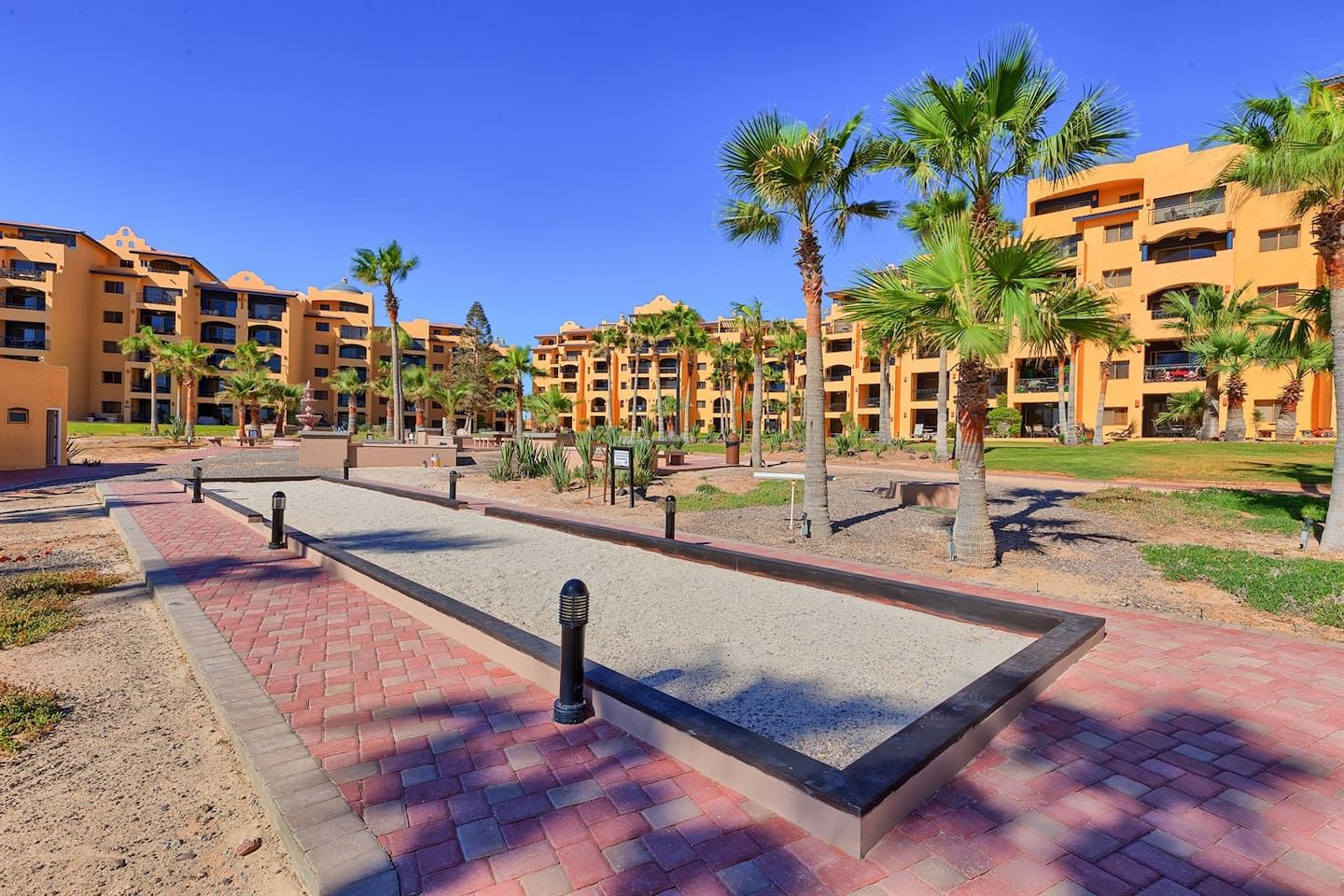 A courtyard with a rectangular pool, palm trees, and a building with balconies.