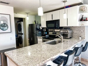 A modern kitchen with granite countertops, stainless steel appliances, and a bar area with bar stools. - 2BDR Remodeled penthouse / Sandy Beach+ beach gear (Puerto Peñasco)