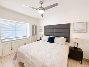 Ein Schlafzimmer mit einem Bett, einem Nachttisch, einem Deckenventilator und einem Fenster mit Jalousien.