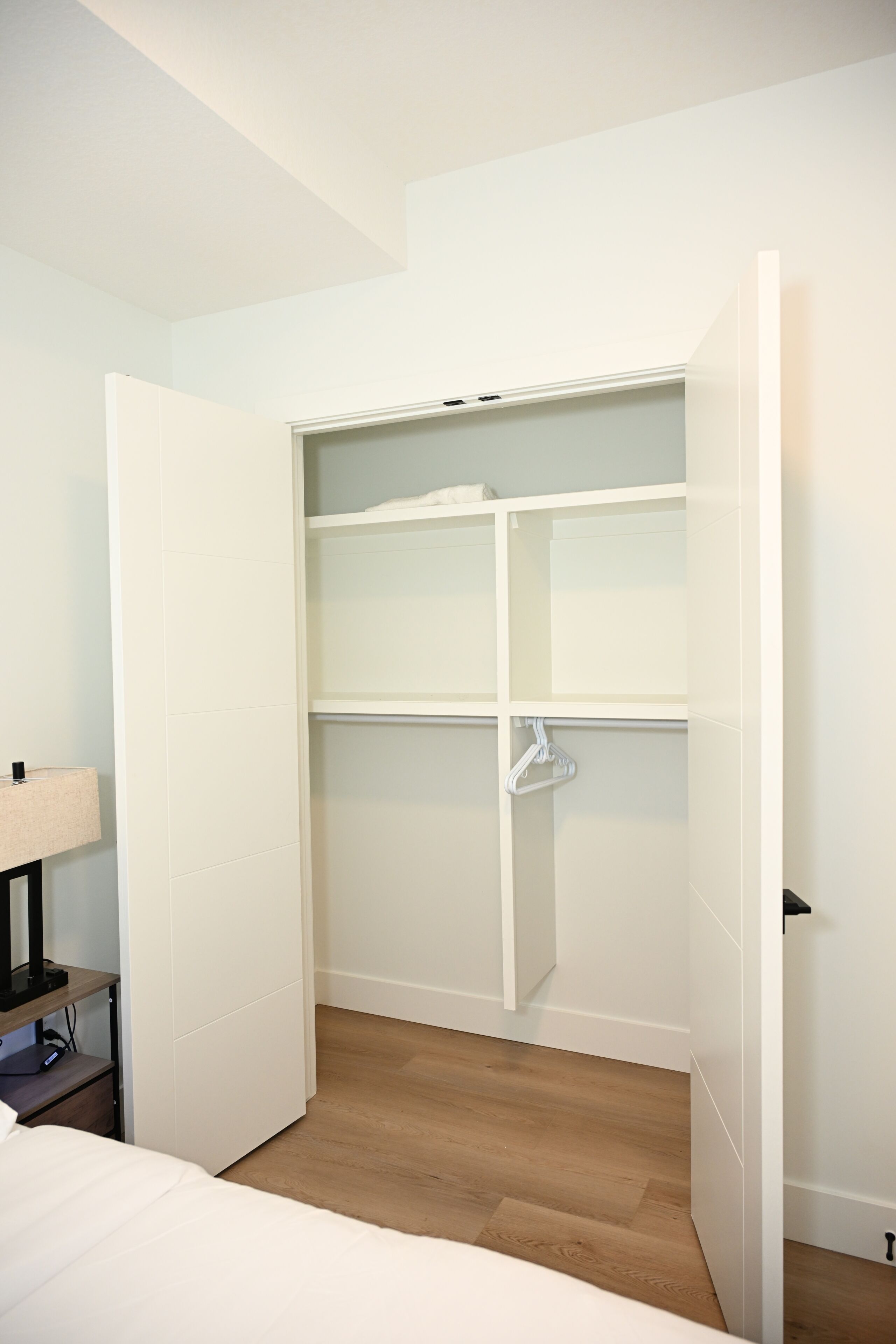 A room with a white closet, a bed, and a nightstand with a lamp.