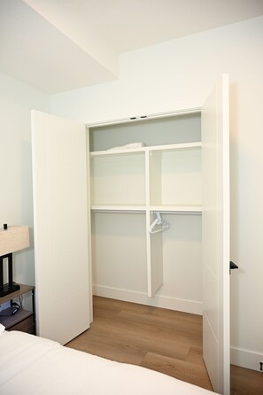 Ein Zimmer mit einem weißen Kleiderschrank, einem Bett und einem Nachttisch mit Lampe.