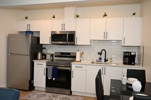 A modern kitchen with stainless steel appliances, white cabinets, and a dining area with a black chair and table. - Luxury 2BR Apartment | Relax, Unwind, Indulge (Edmonton)