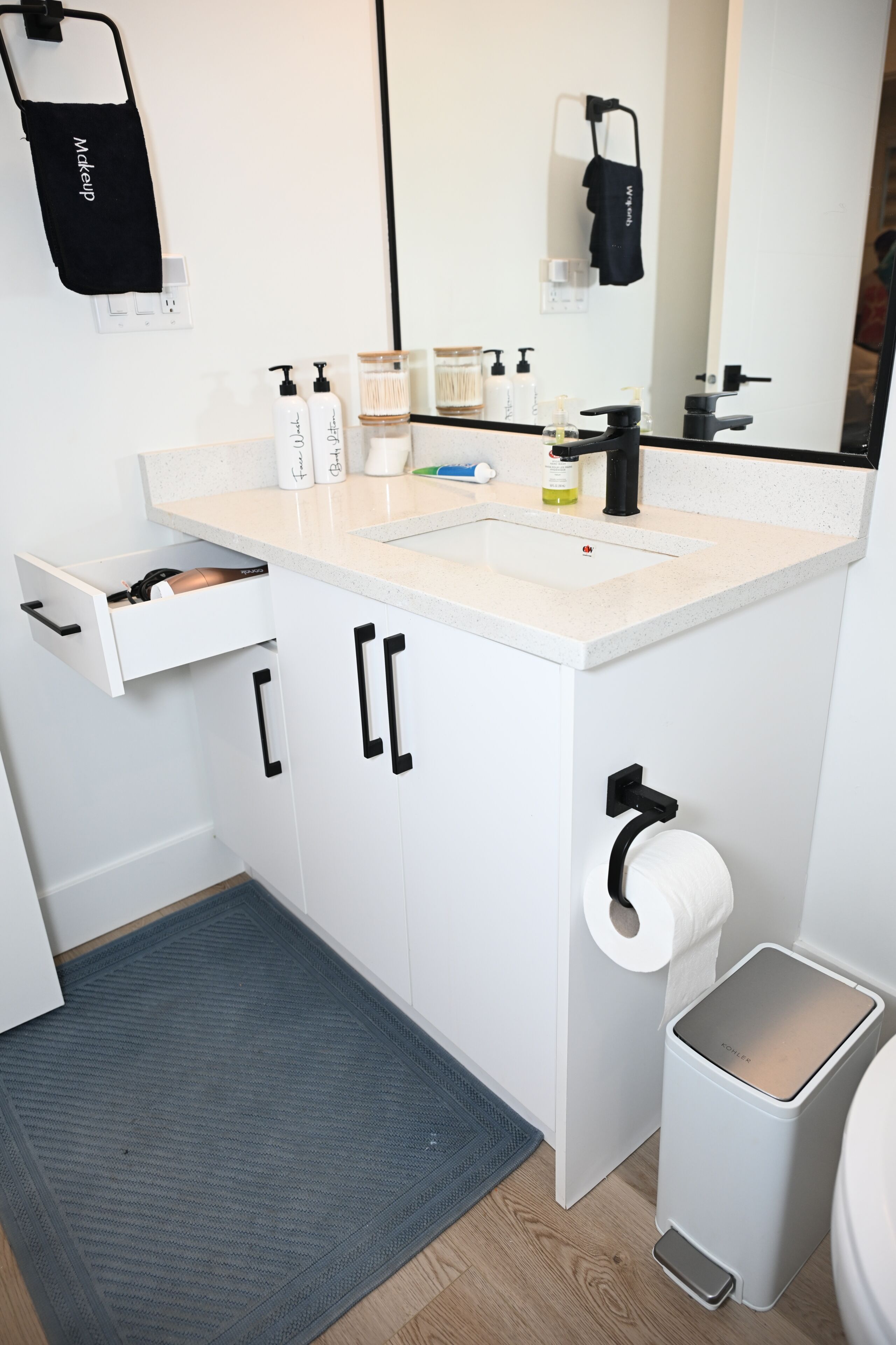 Une salle de bain moderne avec un lavabo blanc, un robinet noir et une serviette suspendue à un porte-serviettes noir.
