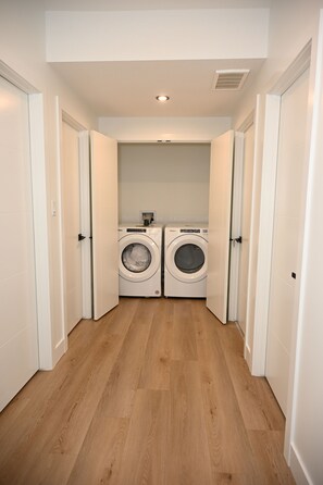 A laundry room with two front-loading washers and dryers, wooden flooring, and white walls. - Luxury 2BR Apartment | Relax, Unwind, Indulge (Edmonton)