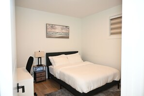 A bedroom with a bed, bedside table, lamp, and a painting on the wall. - Luxury 2BR Apartment | Relax, Unwind, Indulge (Edmonton)