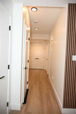 A hallway with wooden flooring, white walls, and doors leading to individual rooms. - Luxury 2BR Apartment | Relax, Unwind, Indulge (Edmonton)