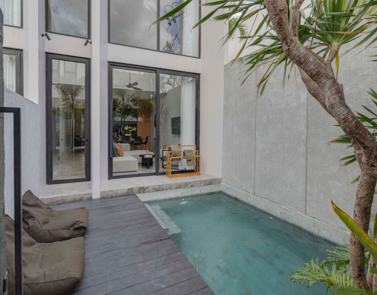 A modern building with a pool, wooden deck, and a seating area with cushions.