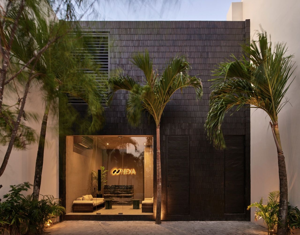 A modern building with a dark facade, a glass entrance, and a visible logo 'NEXA'.