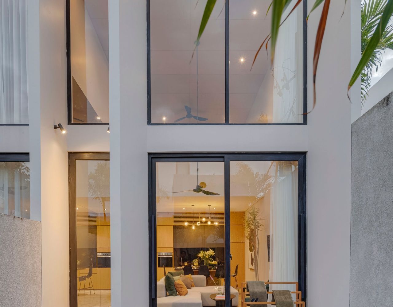 A modern interior with a glass partition, a ceiling fan, and a dining area visible through the glass.
