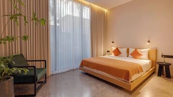 A modern hotel room with a bed, a chair, a potted plant, and a nightstand.