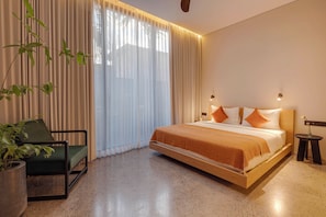 Una habitación de hotel moderna con cama, una silla, una planta en maceta y una mesita de noche.
