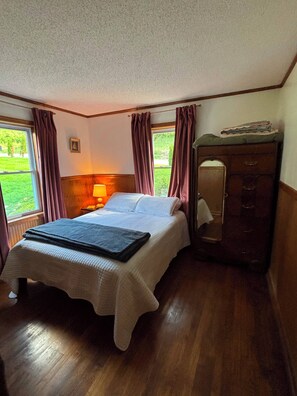 A bedroom with a bed, a dresser, a lamp, and a window with curtains.