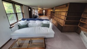 A modern living room with a white sofa, a glass coffee table, and wooden shelving. - Rhododendron Retreat— Dog-Friendly, Sauna, Mountain Views, Appalachian Trail (Roan Mountain)