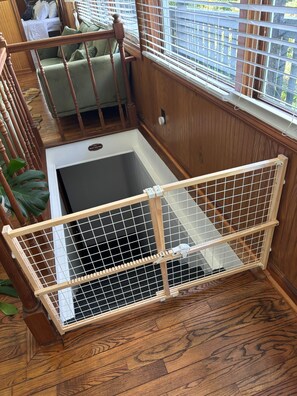 Una escalera de madera con barandilla de metal, un sofá verde y vistas al exterior a través de una ventana con persianas.