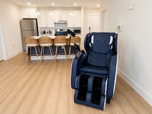 A modern kitchen with white cabinets, a stainless steel refrigerator, a microwave, and a stove. There are four wicker chairs at a dining table. - Luxury North Retreat with Pool and Gym (Naples)