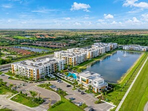 Un ensemble résidentiel comprenant plusieurs immeubles d’appartements, un espace paysager central avec un point d’eau et un parking.