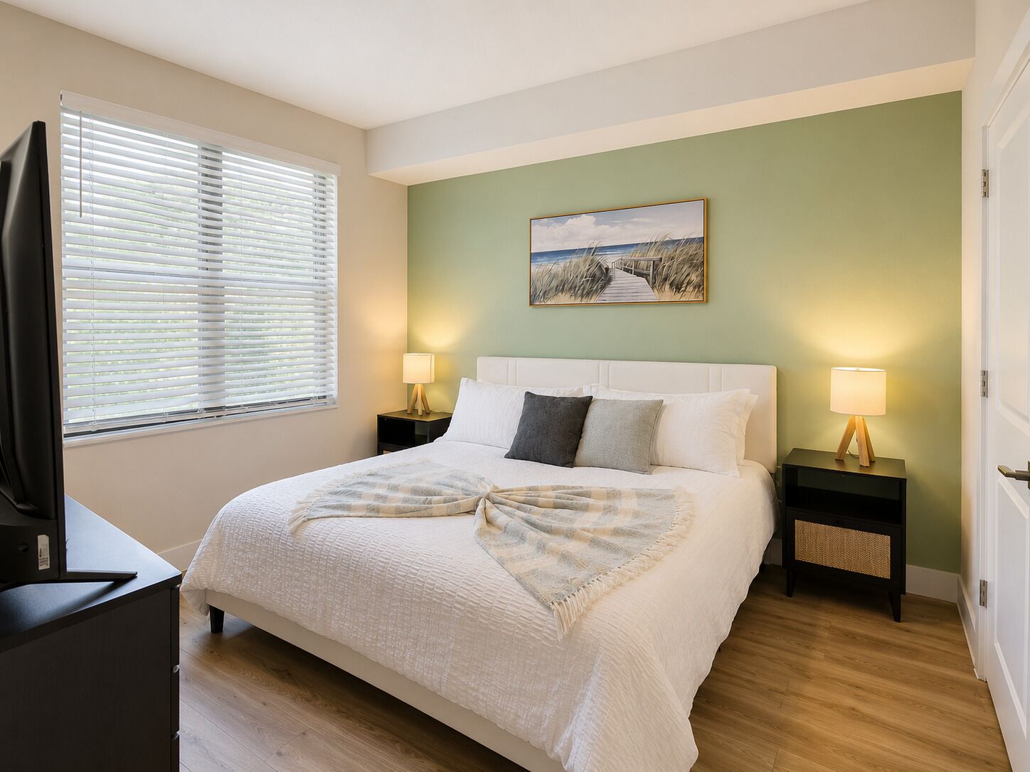 Une chambre à coucher avec un lit, deux tables de chevet avec des lampes, un tableau au mur et un téléviseur posé sur un meuble.