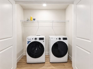 A laundry room with two front-loading washing machines and a metal shelf above. - Luxury North Retreat with Pool and Gym (Naples)