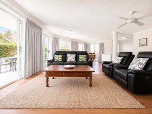 A spacious living room with a large window, a ceiling fan, and a black leather sofa set.