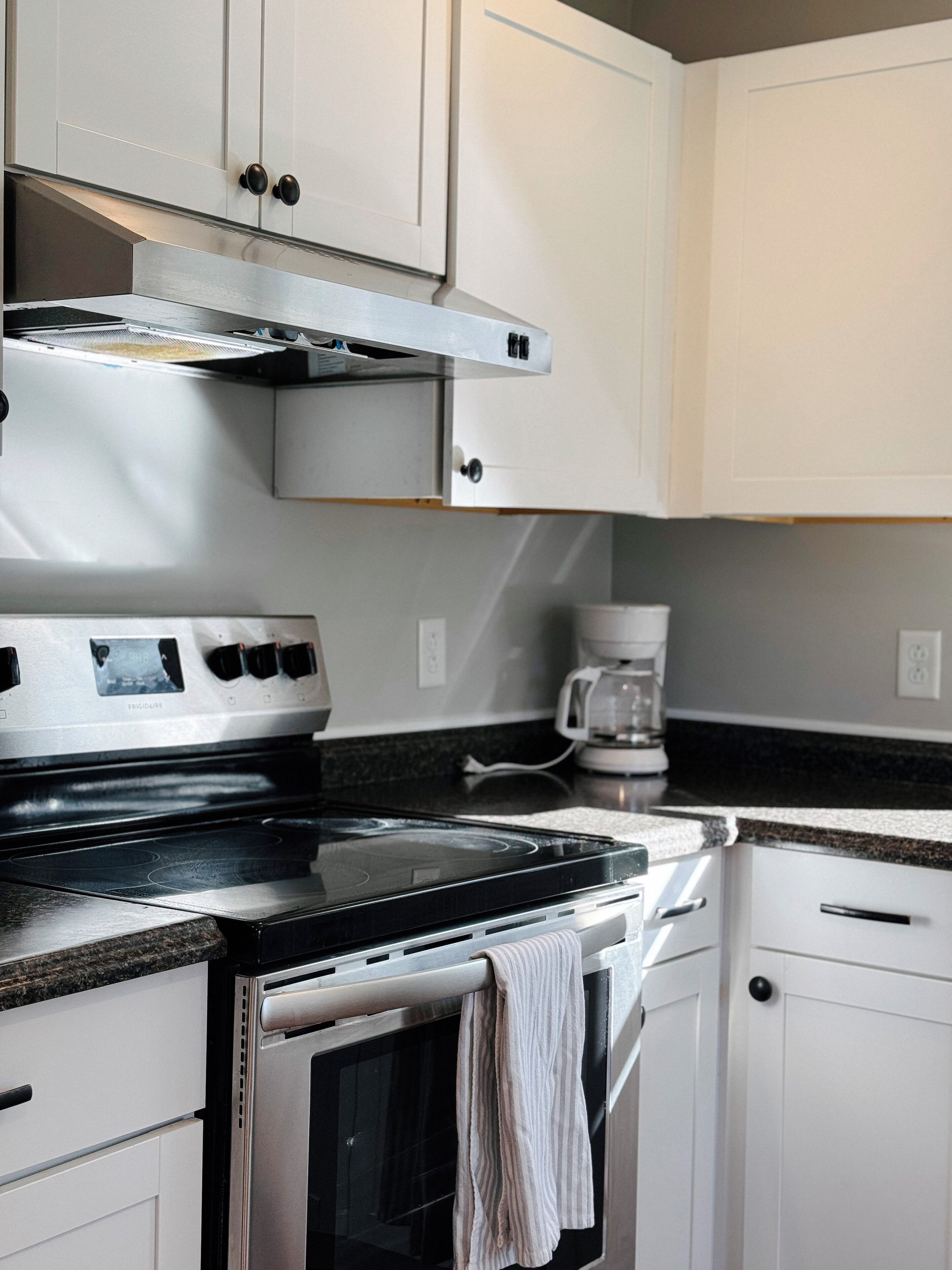 A kitchen with a stainless steel stove, a coffee maker, and white cabinets.