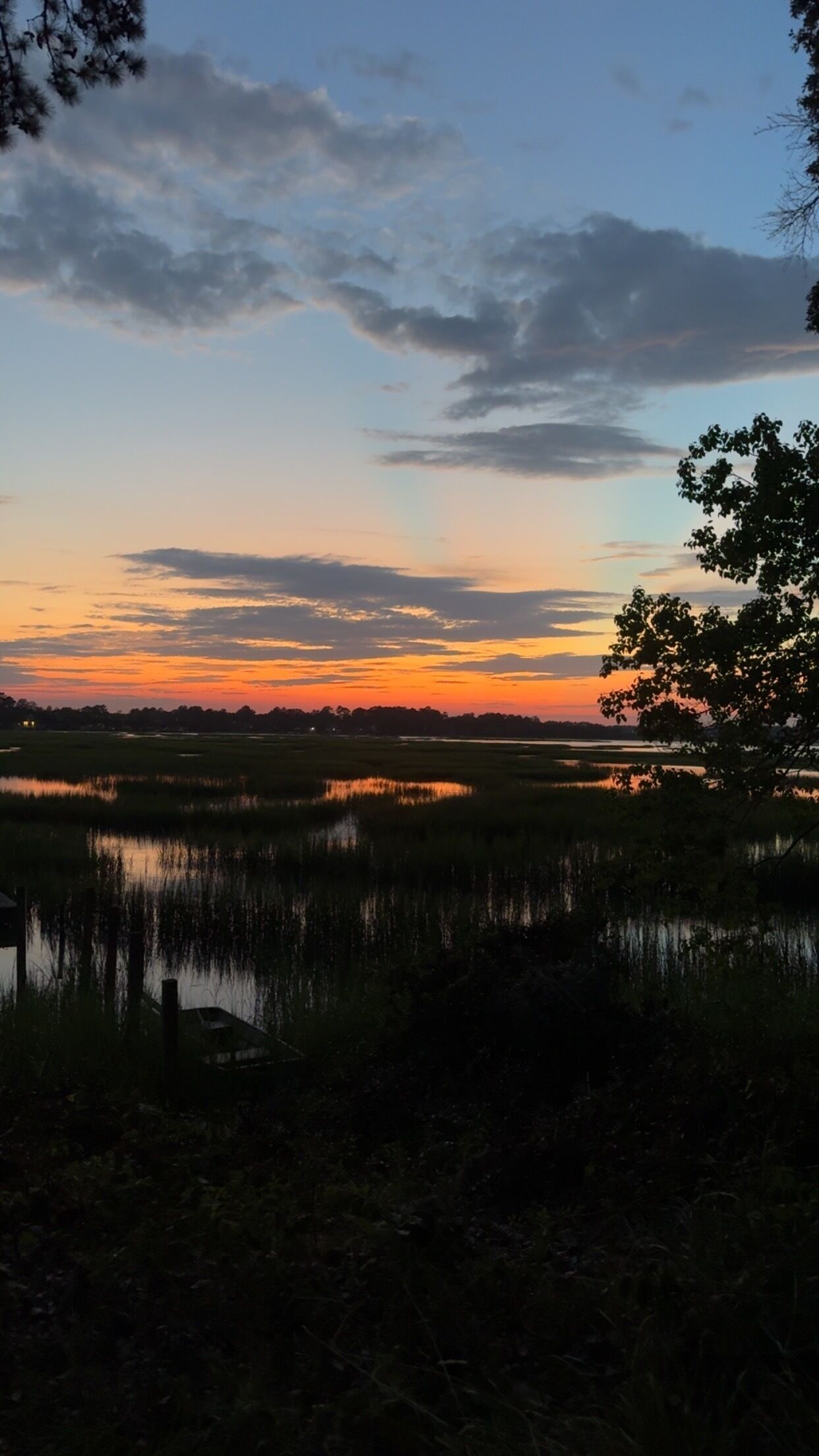 A natural landscape with a body of water, trees, and a sunset sky.