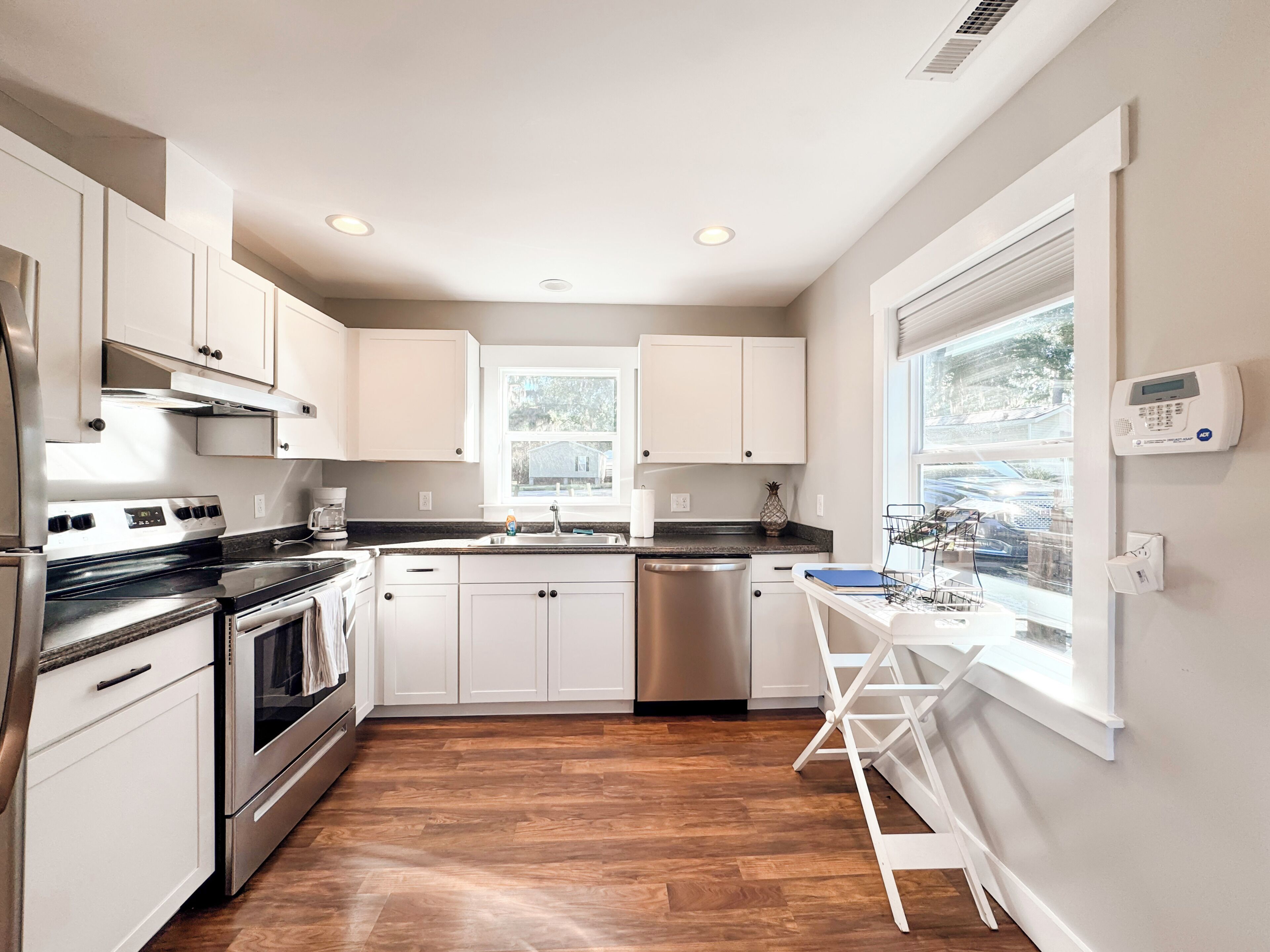 Une cuisine moderne dotée d’appareils électroménagers en acier inoxydable, de meubles blancs et d’un plancher en bois.